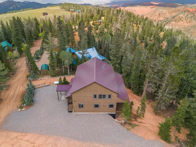 Expansive gravel driveway, wood-sided exterior, burgundy metal roof, covered entry, and surrounding mature trees