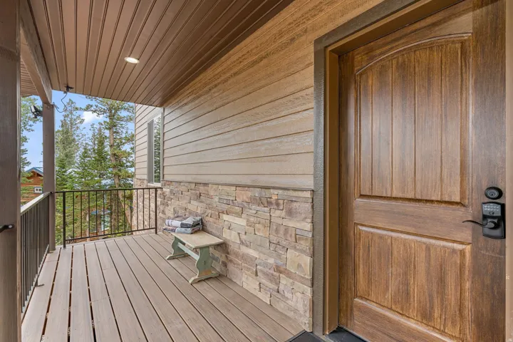 Covered front porch featuring wood-finish siding, stone veneer accents, and wood-finish composite decking