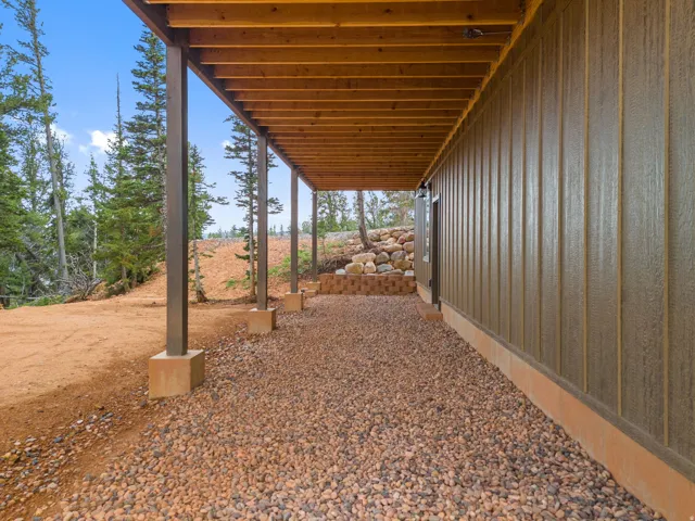 Covered outdoor area featuring exposed wood ceiling joists, support columns with concrete bases, and a gravel surface