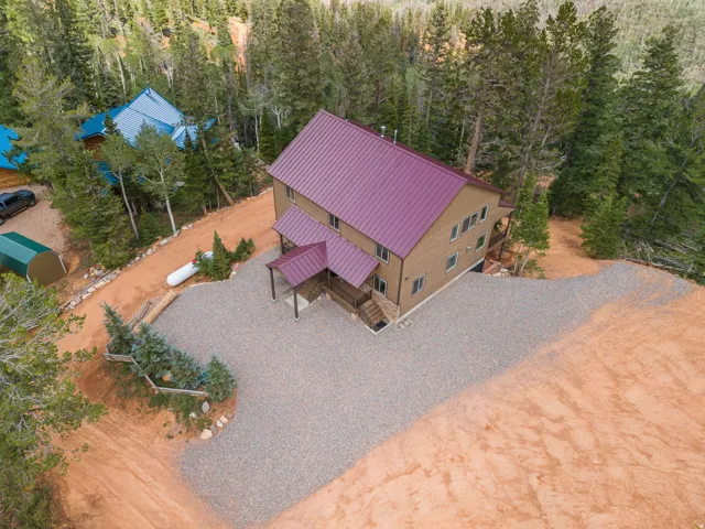 Multi-story residence featuring a maroon metal roof, light brown siding, and a covered entry porch