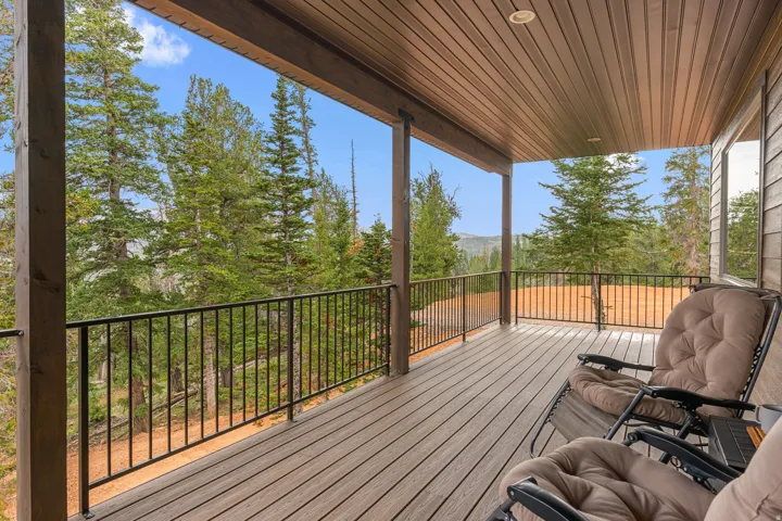 Expansive covered deck with wood-finish decking and black metal railings, set against a backdrop of mature trees and distant hills