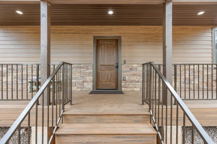 Front porch with wood-finish decking, dark metal railings, and stone veneer accents