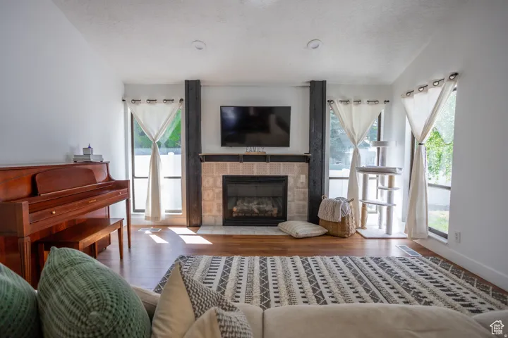 Living area featuring wood-finish flooring, a fireplace with a tiled surround, recessed lighting, and large windows