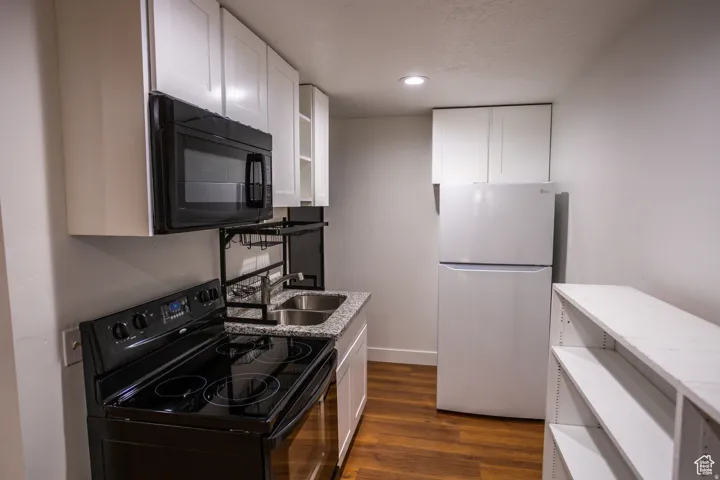 Compact kitchen featuring white cabinetry, a black range with an overhead microwave, a double basin sink, and a white refrigerator