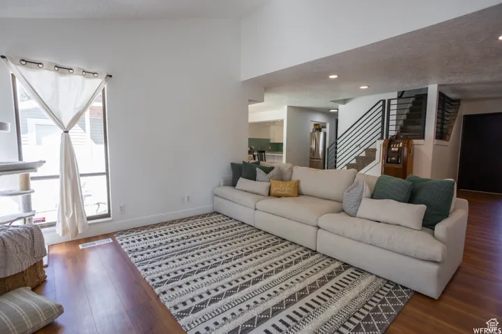 Open-concept living area with wood-finish flooring, vaulted ceiling, recessed lighting, and a modern staircase featuring horizontal metal railings