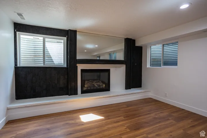 Recessed fireplace with a stone hearth, wood-finish flooring, and two egress windows
