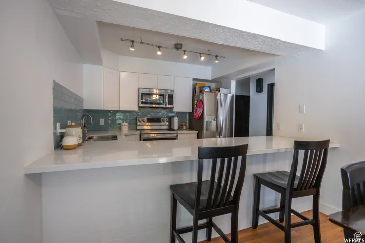 Modern kitchen featuring white cabinetry, a light-toned countertop, stainless steel appliances, and a blue tile backsplash