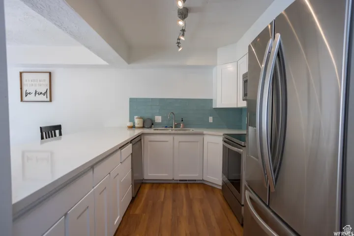Kitchen featuring white cabinetry, light countertops, stainless steel appliances, a light blue tile backsplash, and wood-finish flooring
