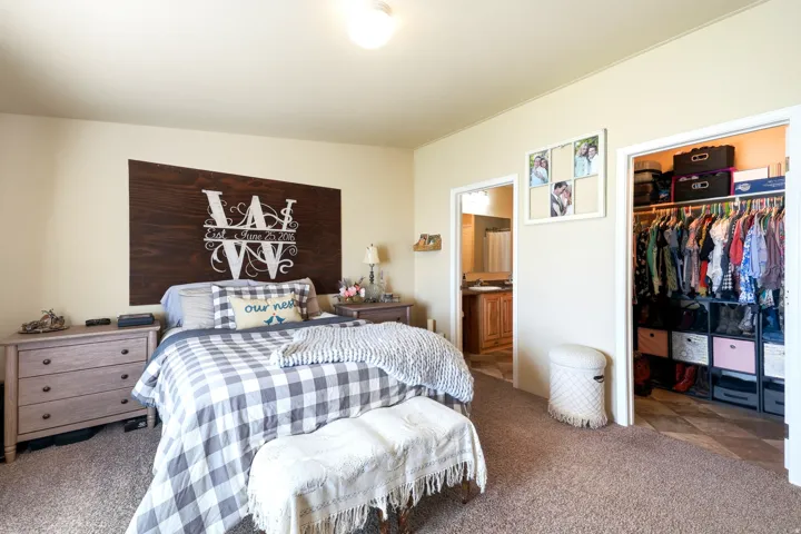 Spacious room featuring neutral wall tones, carpet flooring, a walk-in closet with built-in shelving, and an en-suite bathroom with a wood-finish vanity and integrated sink