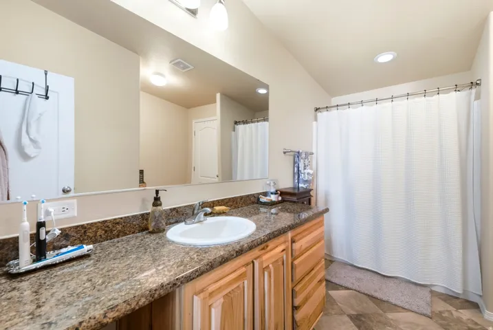 Granite-style countertop with integrated sink, wood cabinetry, large vanity mirror, and recessed ceiling lighting