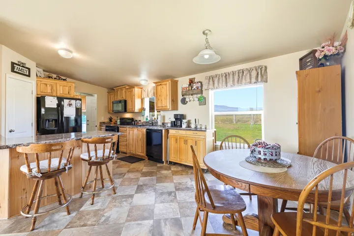 Bright, open kitchen and dining area featuring warm wood cabinetry, stainless steel appliances, tile flooring, and abundant natural light from large windows overlooking expansive countryside vistas