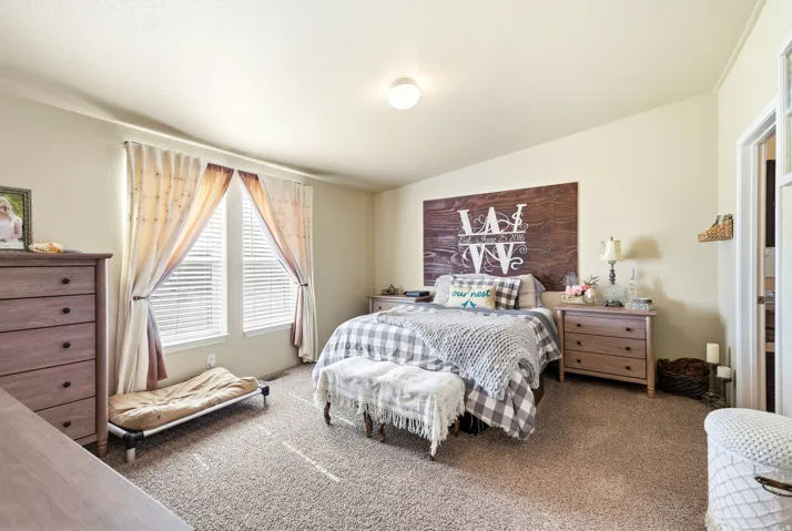 Spacious primary bedroom featuring carpeted flooring, dual nightstands with wood-finish construction, an accent wall with shiplap detailing, large windows with layered window treatments, and abundant natural light from recessed ceiling fixtures