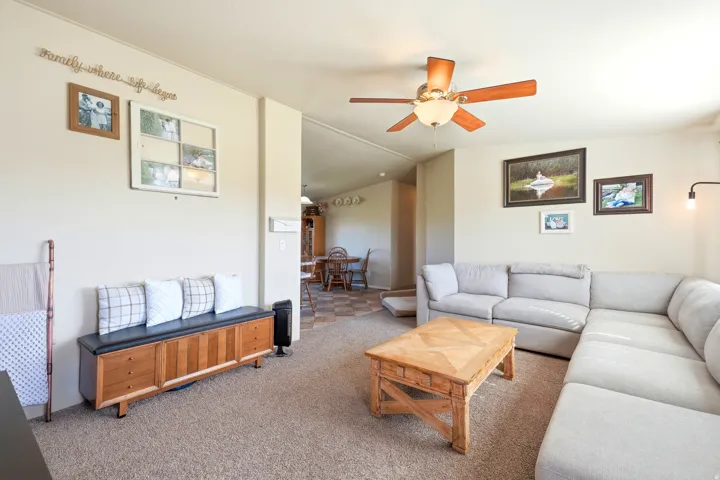 Spacious living area featuring a sectional seating arrangement, wood-finish coffee table, and ceiling fan with integrated lighting