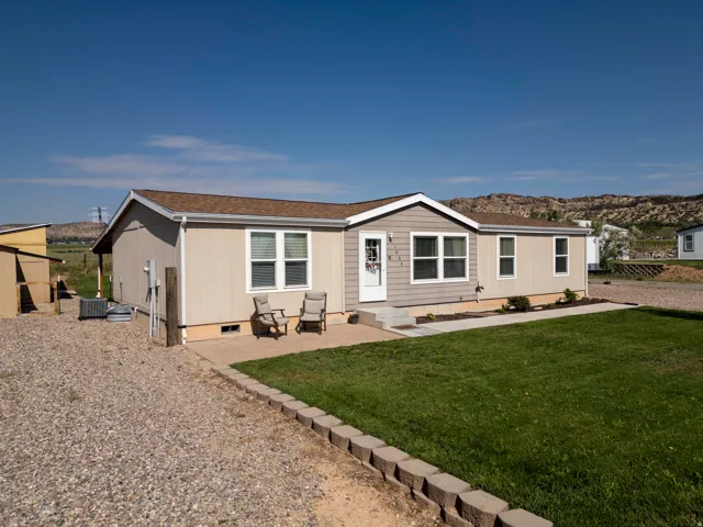 Single-story residence featuring a neutral exterior, front patio with paver stones, landscaped garden beds, a gravel driveway, and a detached storage shed