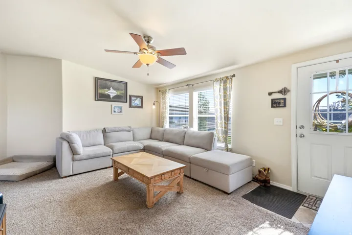 Vaulted ceiling with a ceiling fan, multiple windows with blinds, a white entry door with glass panels, and neutral-toned wall paint