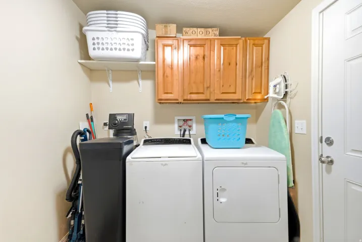 Dedicated laundry room featuring side-by-side washer and dryer, wood-finish cabinetry with ample storage, shelving for supplies, and direct exterior access