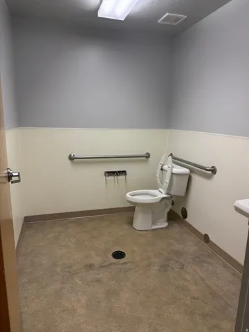 Commercial restroom with two-tone wall treatment, white toilet, and multiple grab bars