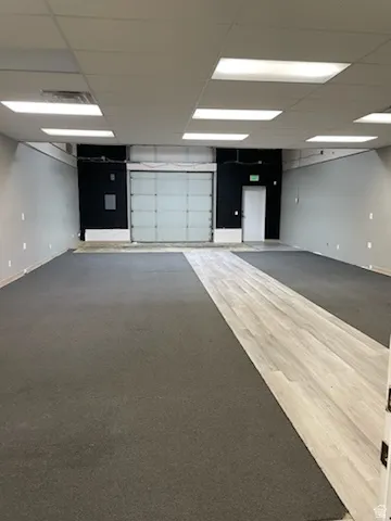 Spacious interior featuring a roll-up door, dropped ceiling with integrated lighting, wood-finish flooring, and carpeting