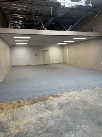 Spacious commercial interior featuring a mix of concrete and carpeted flooring, exposed ceiling infrastructure, and recessed lighting