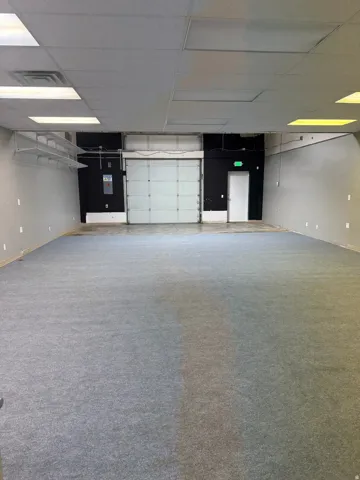 Spacious commercial interior featuring a roll-up garage door, supplemental personnel door, and drop ceiling with integrated lighting