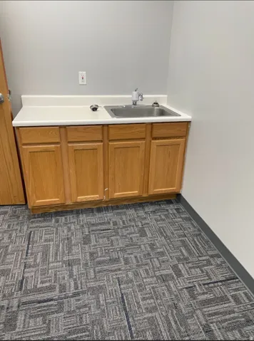 Wood-finish cabinetry with a laminate countertop, stainless steel sink, and patterned carpet flooring