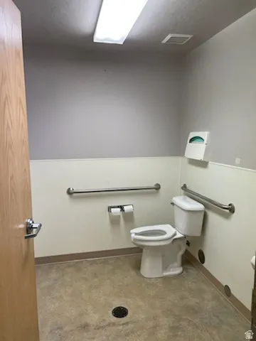 Restroom featuring a neutral color palette, commercial-grade flooring, wall-mounted grab bars, and a flush-mounted ceiling light fixture