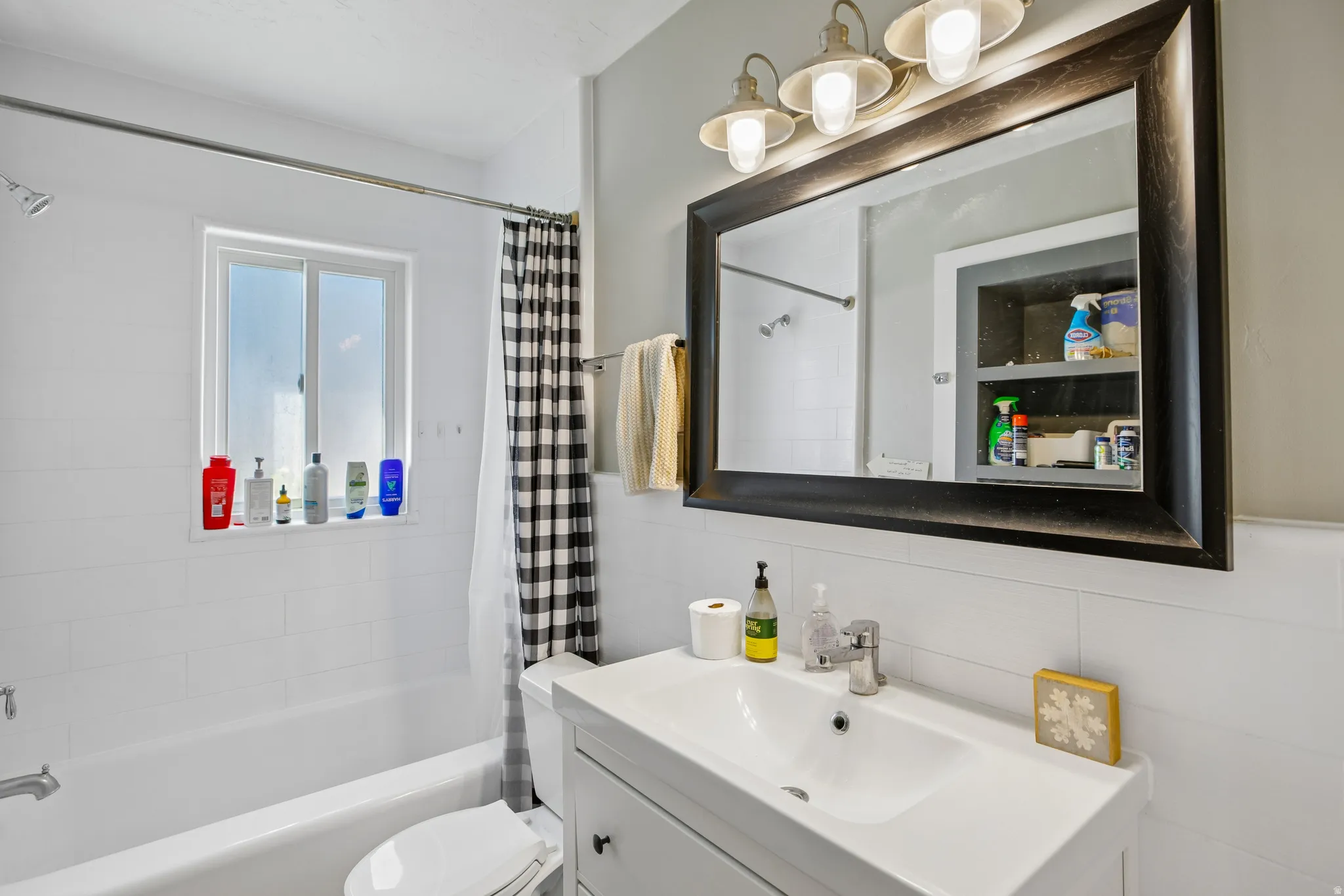 White subway tile surround, white vanity with integrated sink, chrome faucet, and framed mirror with integrated lighting