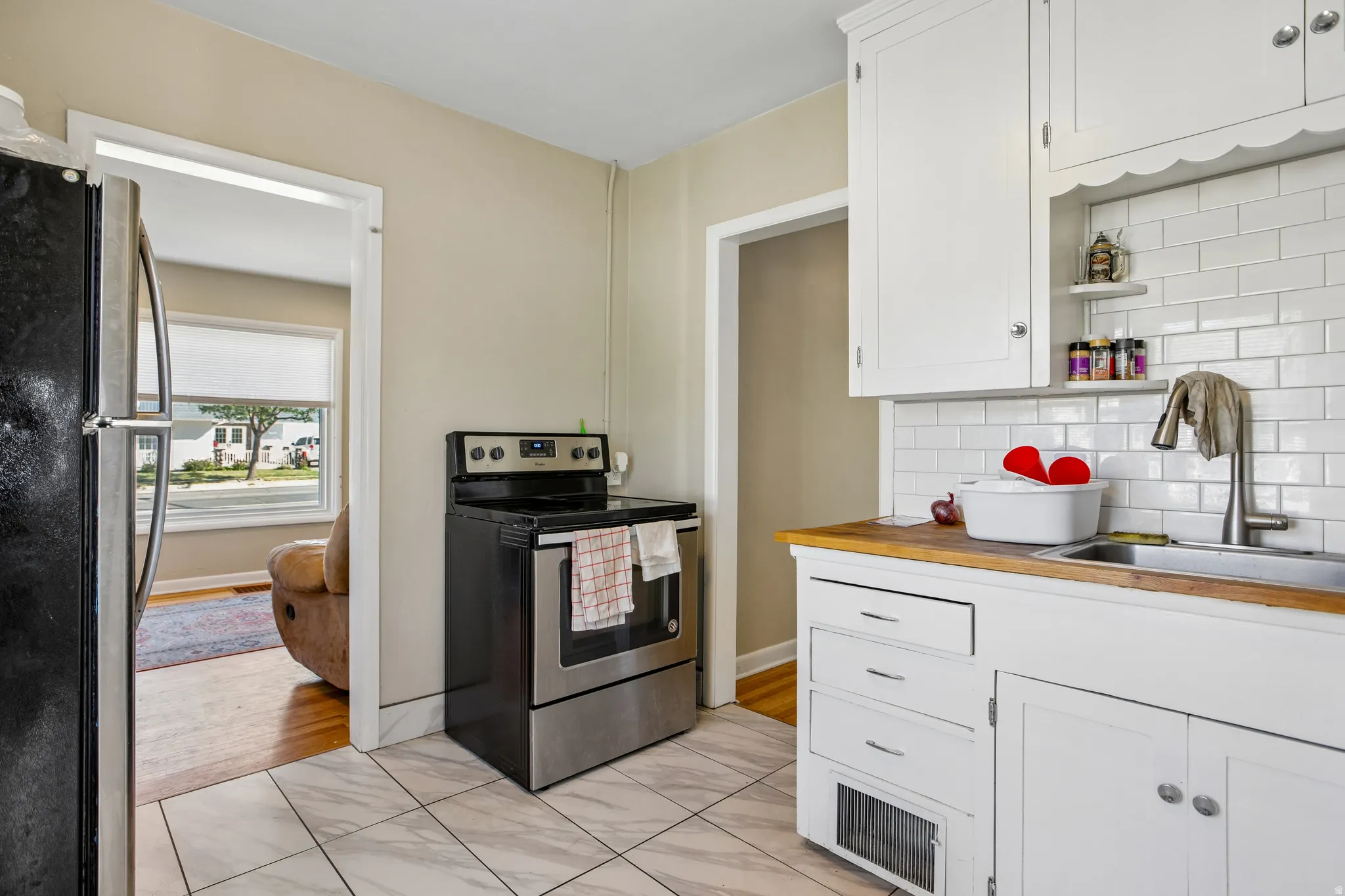 Kitchen featuring white subway tile backsplash, white cabinetry, wood-finish countertops, and a stainless steel oven