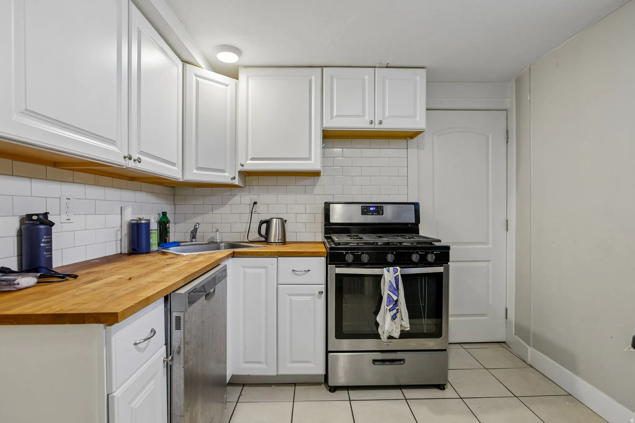 White cabinetry with decorative pulls, subway tile backsplash, wood-finish countertops, and stainless steel appliances