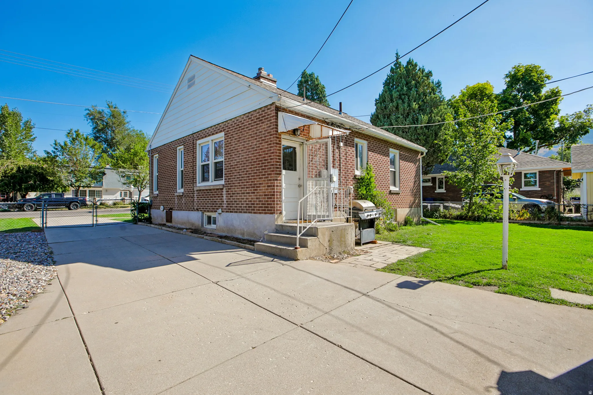 Brick exterior, concrete driveway, front porch with metal railing, grassy yard, and mature trees