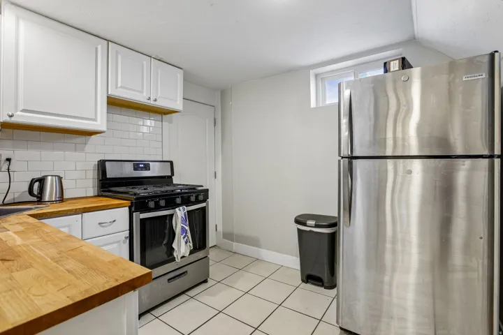White upper and lower cabinetry, wood-finish countertops, subway tile backsplash, stainless steel gas range, and stainless steel refrigerator