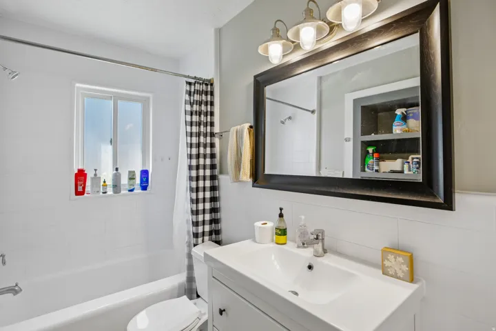 White subway tile surround, white vanity with integrated sink, chrome faucet, and framed mirror with integrated lighting