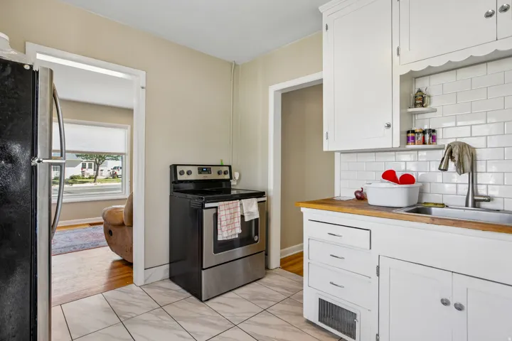 Kitchen featuring white subway tile backsplash, white cabinetry, wood-finish countertops, and a stainless steel oven