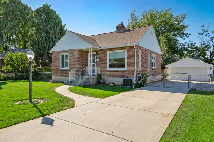 Brick exterior with white trim, concrete driveway, detached garage, and a curved concrete walkway