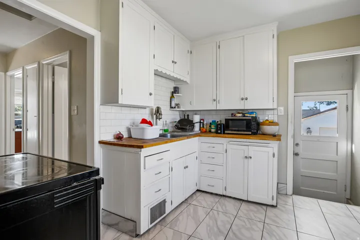 White cabinetry with ample storage, butcher block countertops, subway tile backsplash, and ceramic tile flooring