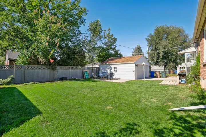 Expansive lawn area, detached garage with overhead door, brick exterior, lattice-top fencing, and concrete patio