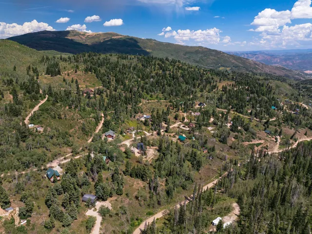 Expansive mountainous terrain featuring dense forests, multiple structures, and winding unpaved roads