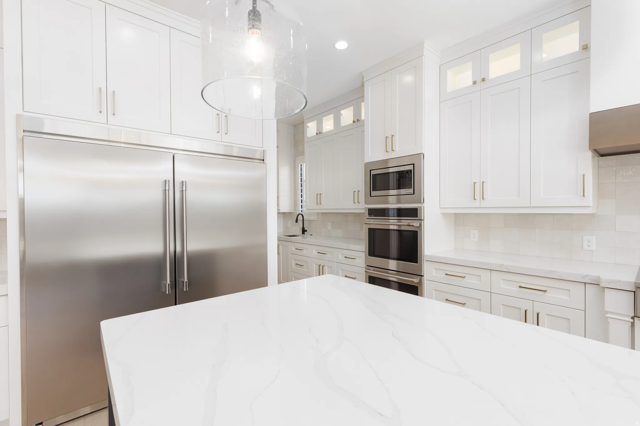 Gourmet kitchen featuring a large white island, stainless steel appliances, white cabinetry with gold hardware, a built-in microwave, and a double oven
