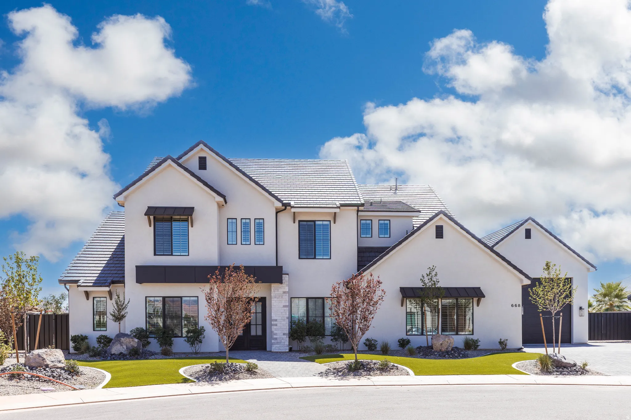 Contemporary stucco exterior with a multi-gabled roofline, black-framed windows, artificial turf landscaping, and a paver driveway