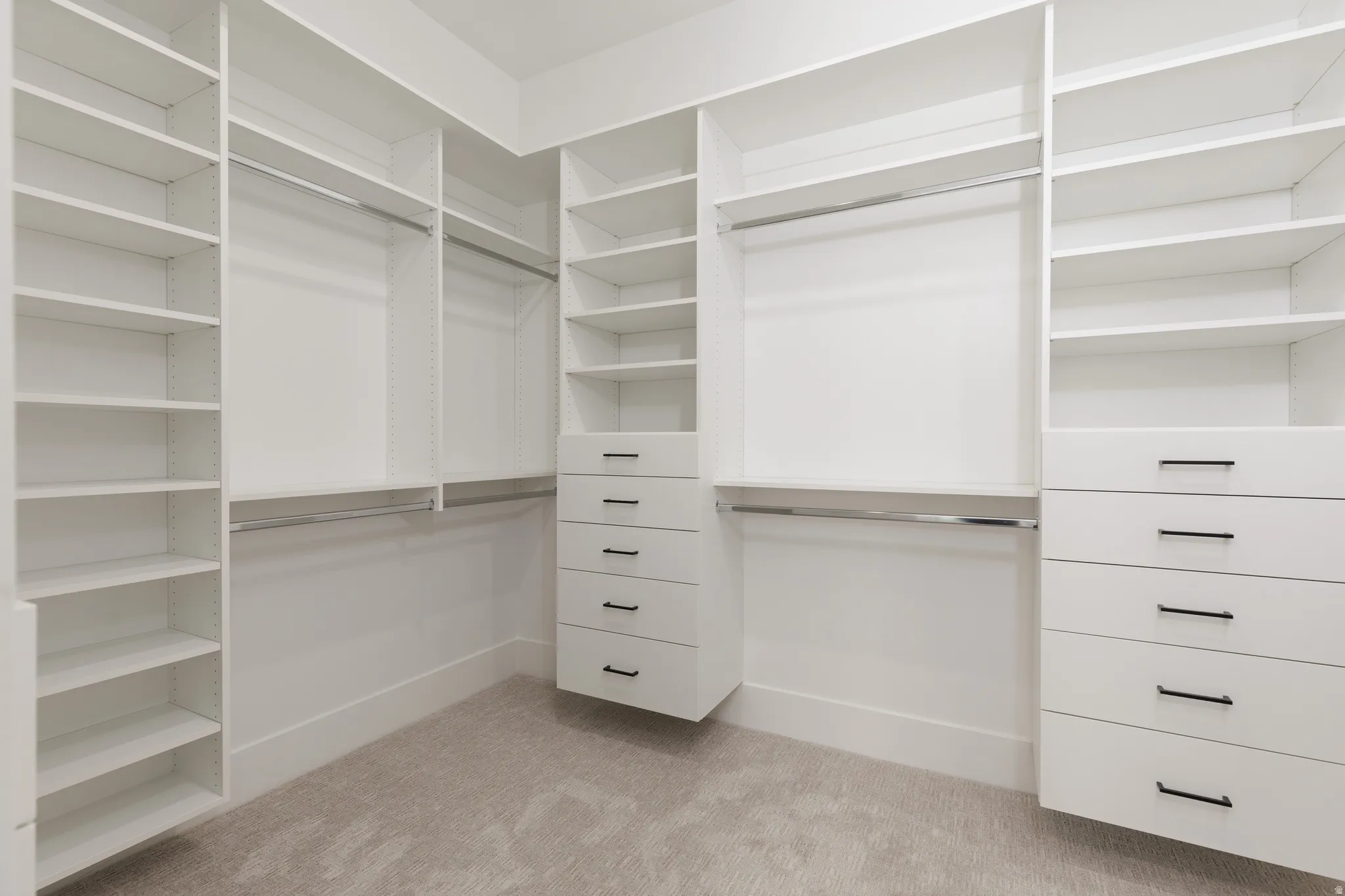 Custom closet system featuring multiple shelving units, hanging rods, built-in drawers with dark hardware, and light-toned carpeting