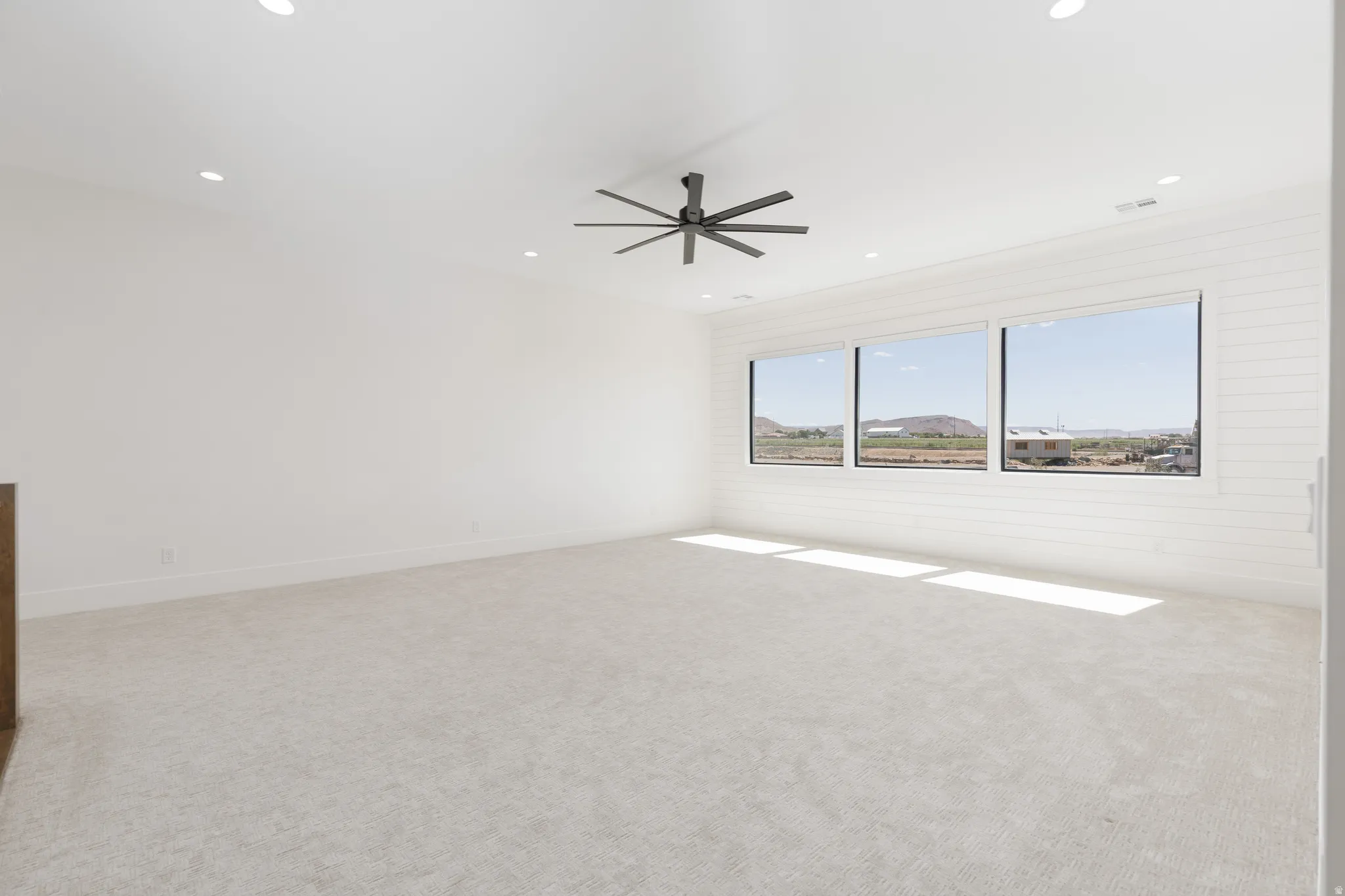 Spacious room featuring light-colored carpeting, recessed lighting, and a modern ceiling fan