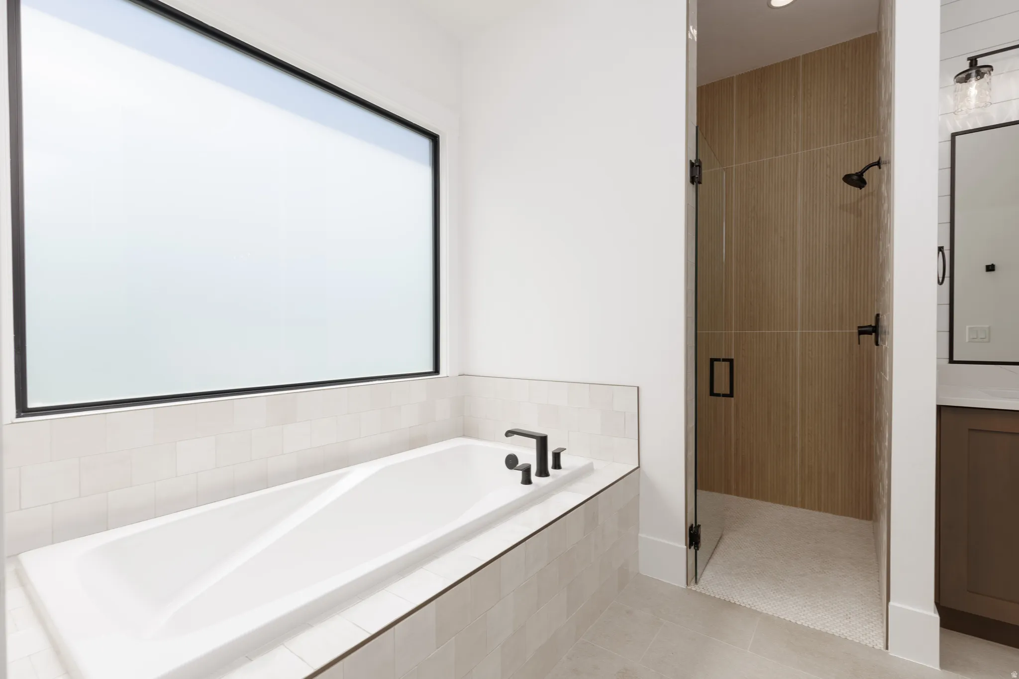 Built-in soaking tub with matte black fixtures, set against a tiled surround and a large horizontal window