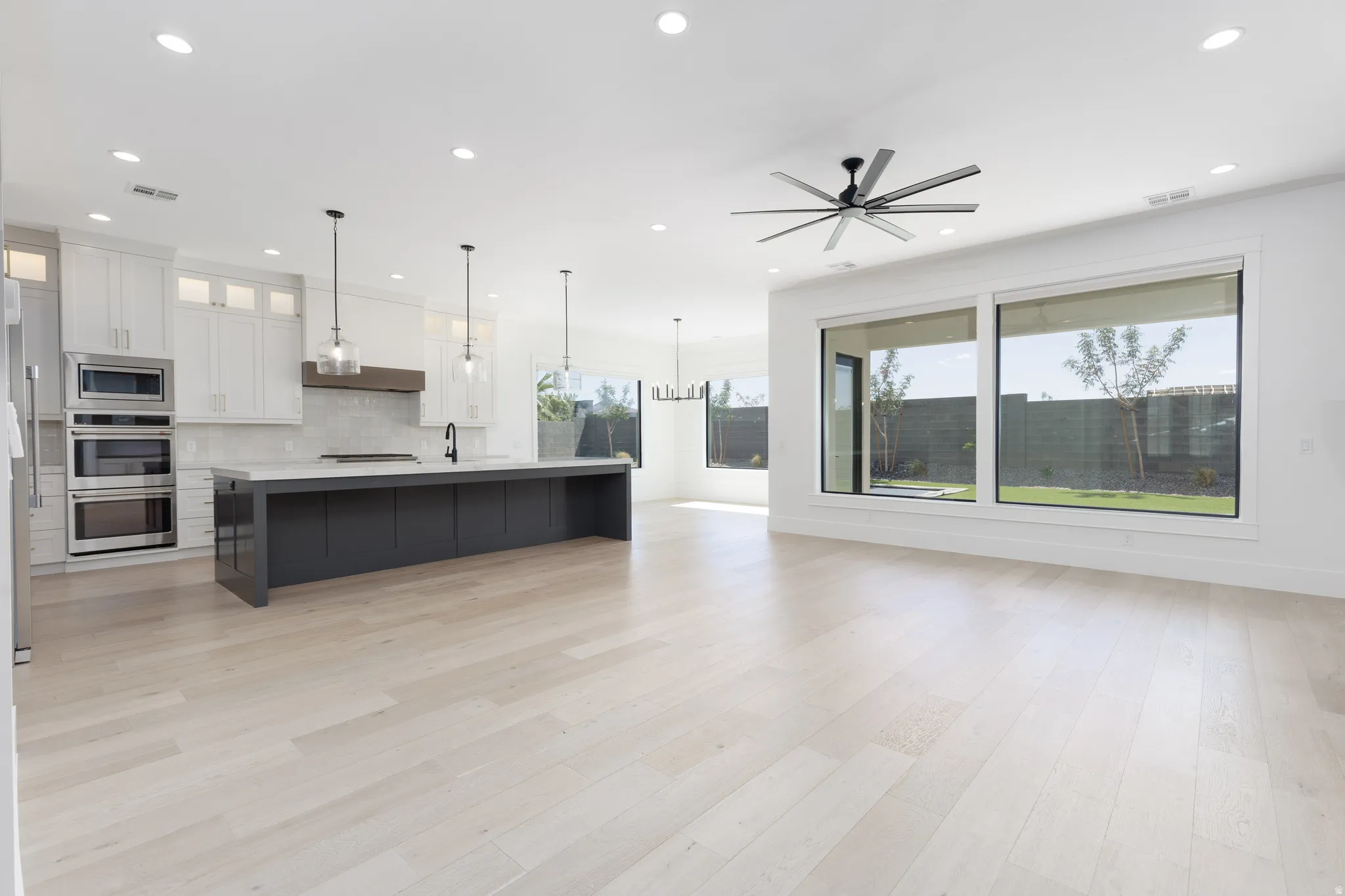Open-concept living area with light wood-finish flooring, recessed lighting, and a contemporary ceiling fan