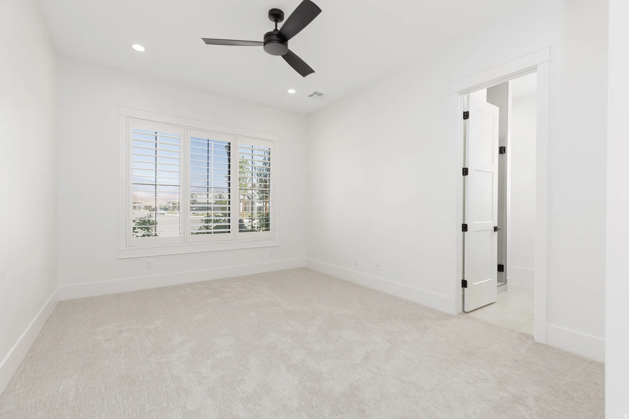 Recessed lighting, ceiling fan, and white plantation shutters complement the neutral wall finishes and plush carpeting