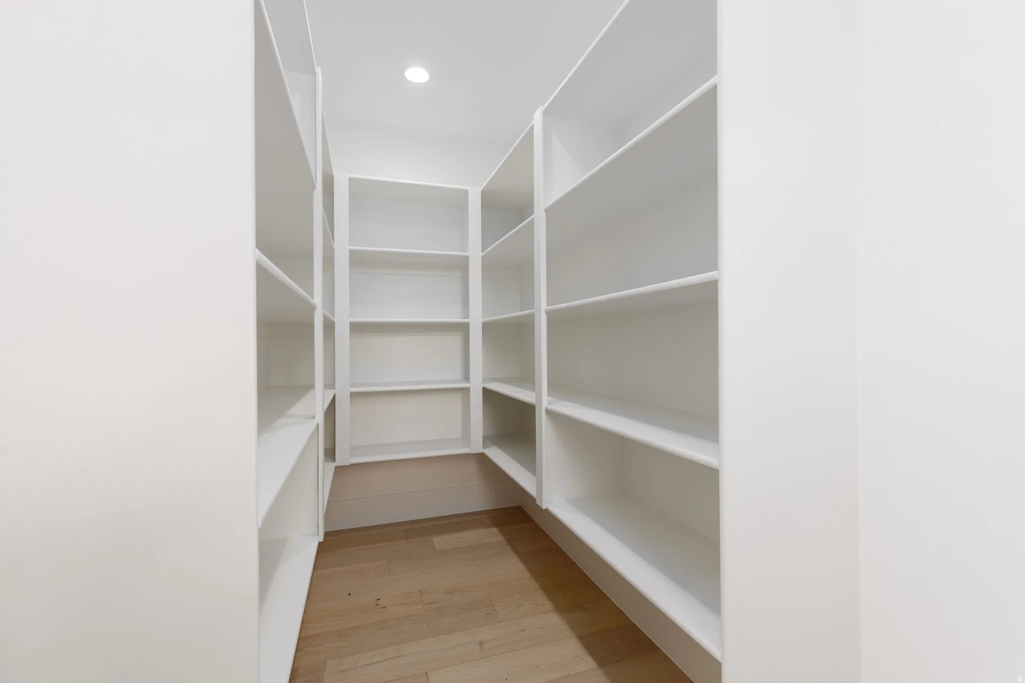 Walk-in pantry with extensive built-in shelving, recessed lighting, and wood-finish flooring