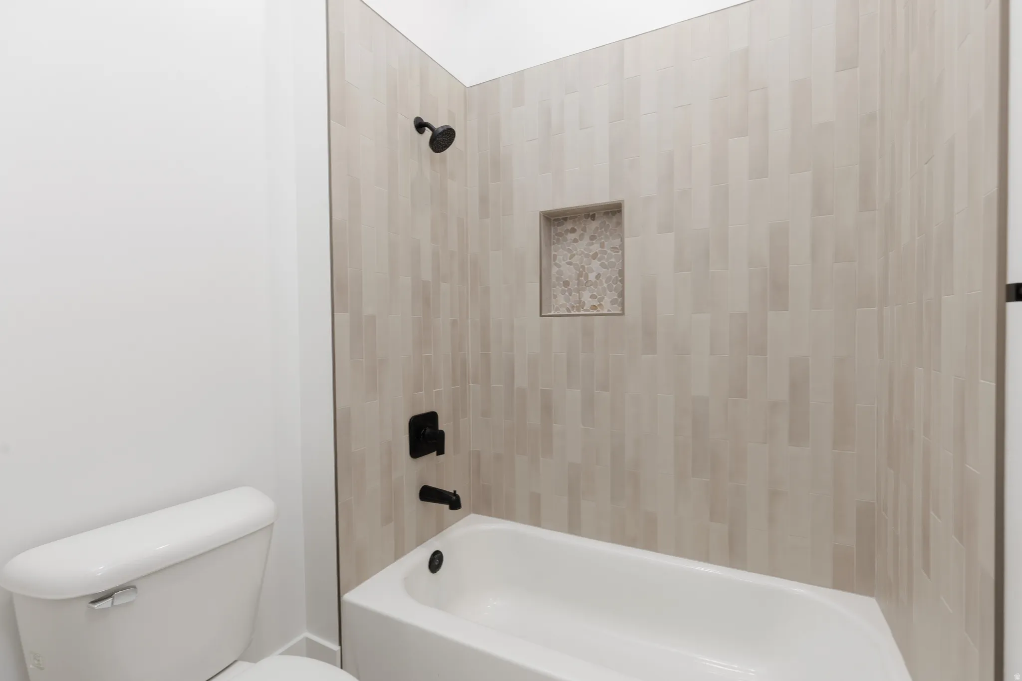 Bathtub with matte black fixtures, an integrated niche, and vertical-stacked tile surround