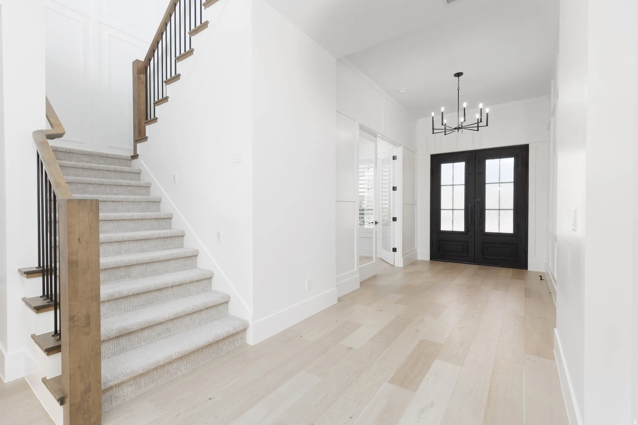 Light wood-finish flooring, a carpeted staircase with wood and metal railings, and a black double-door entry with glass panels