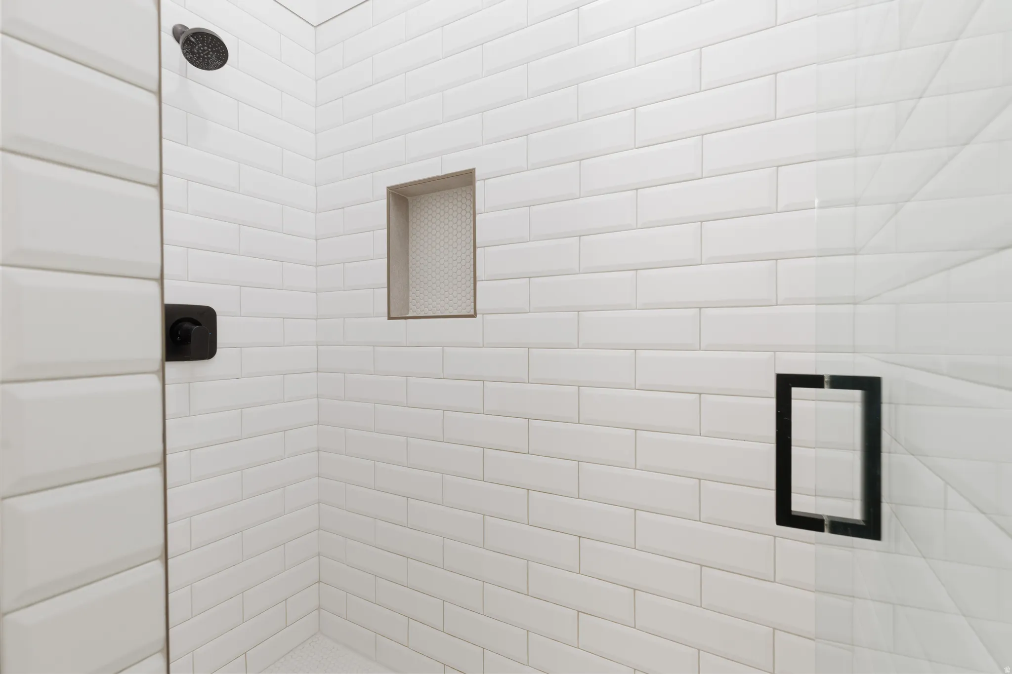 Shower enclosure featuring white subway tile, a built-in shower niche, a matte black shower head, and a frameless glass door with a matte black handle