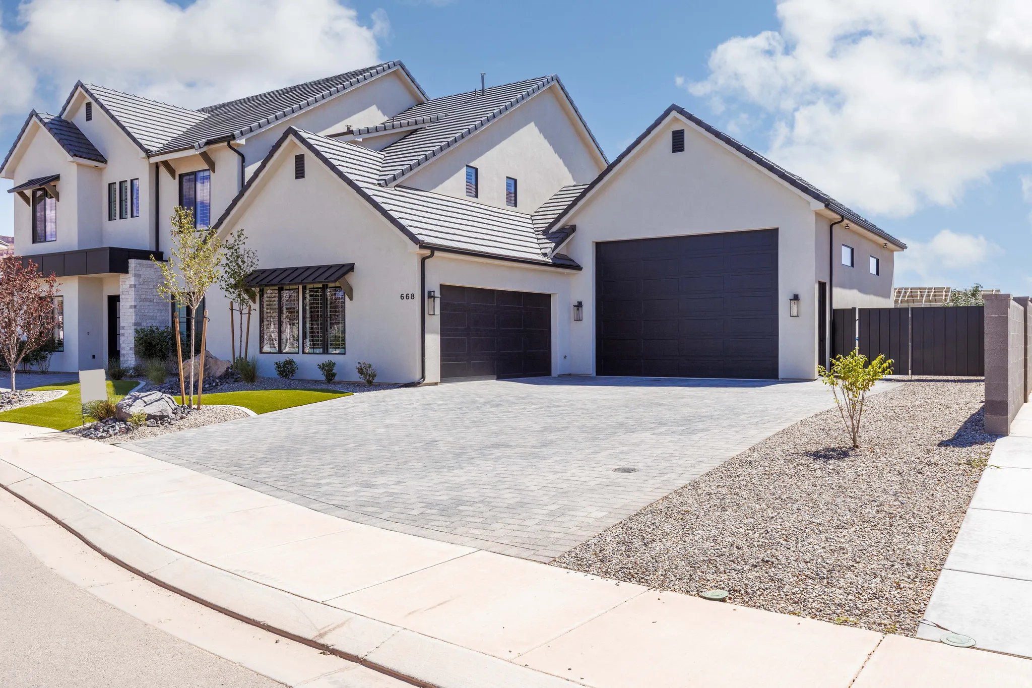 Modern stucco exterior with a multi-gabled roofline, two dark-toned garage doors, a paved driveway, and mature landscaping