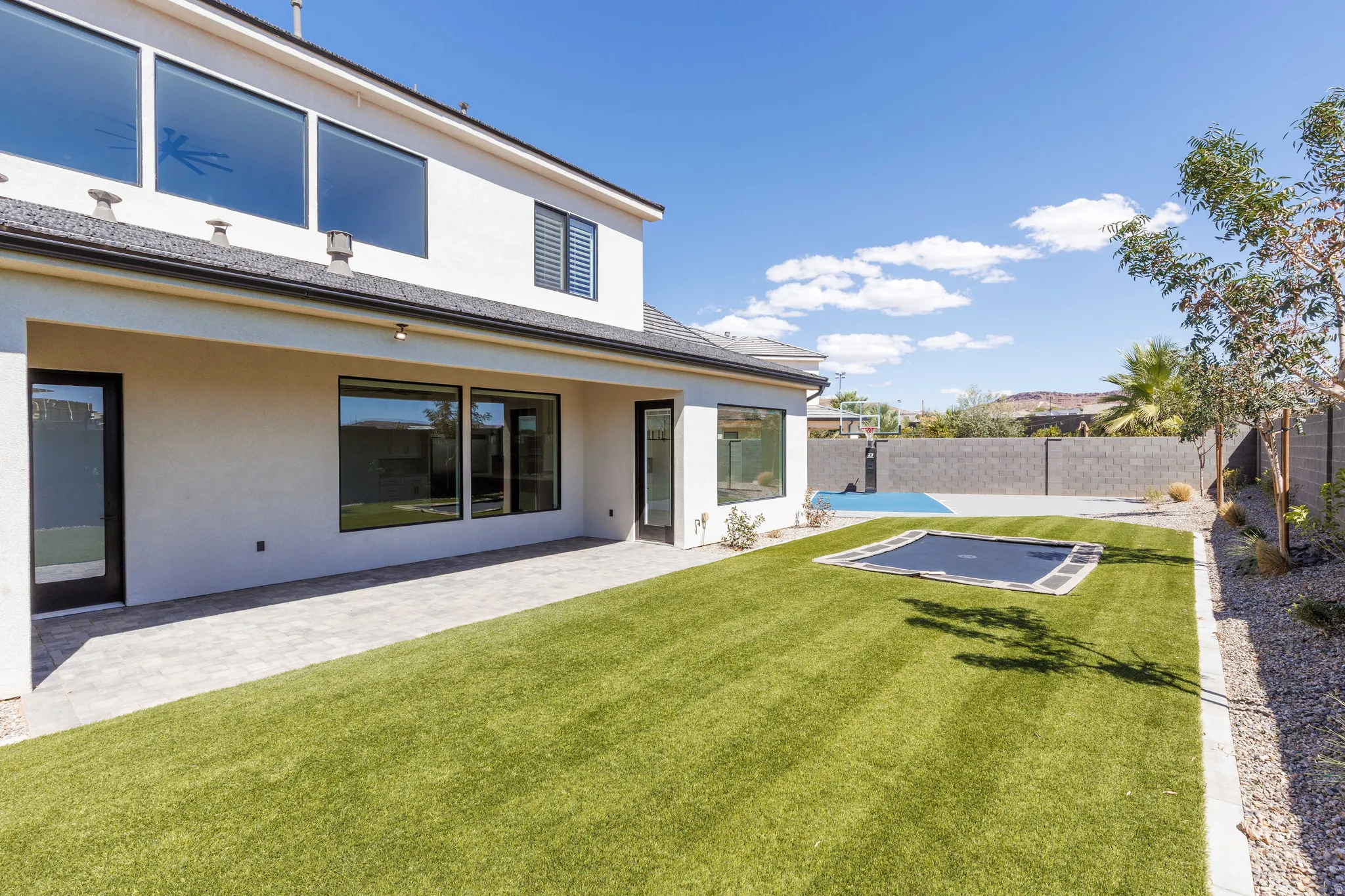 Private backyard featuring a paved patio, expansive green lawn, and integrated trampoline